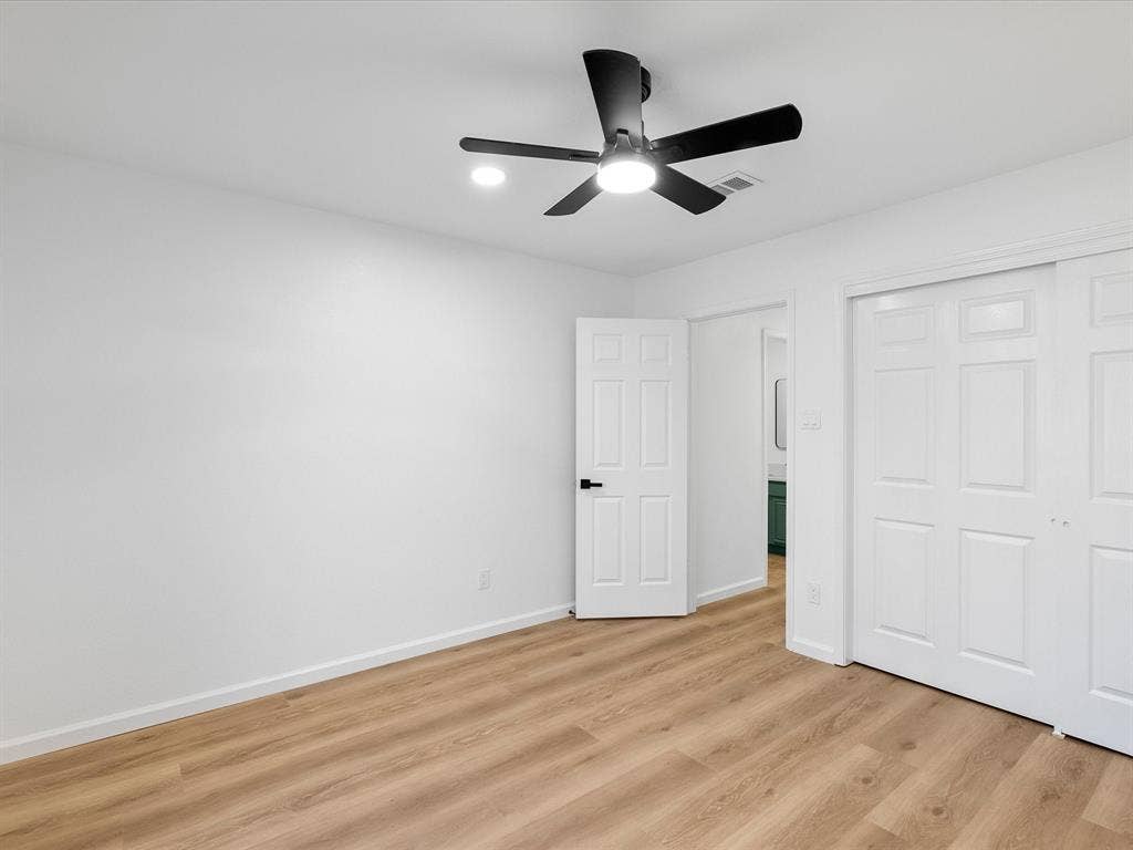 Wood-finish flooring, white walls, and a black ceiling fan with integrated lighting