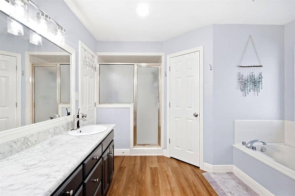 506 Amy Jo Circle, Aubrey, TX 76227 Bathroom featuring a single vanity with a white countertop, a built-in soaking tub, a shower enclosure with a frosted glass door, and wood-finish flooring
