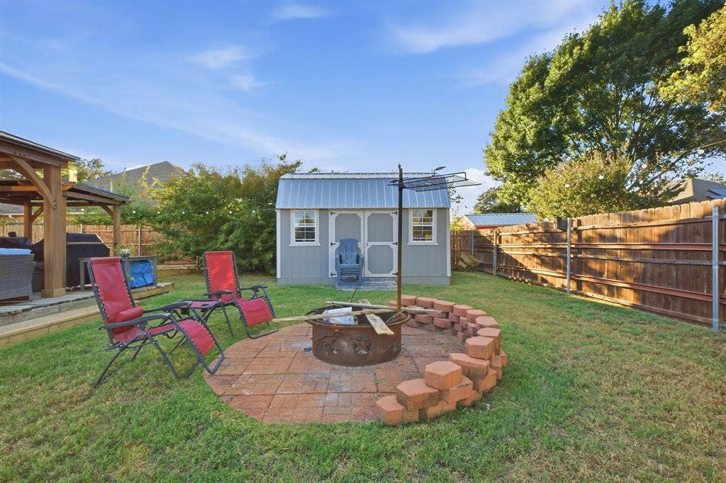 506 Amy Jo Circle, Aubrey, TX 76227 Expansive backyard featuring a fire pit with a paver base, a wooden privacy fence, a storage shed, and a covered patio structure