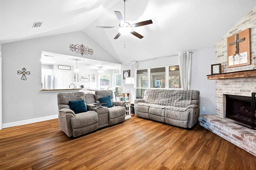 506 Amy Jo Circle, Aubrey, TX 76227 Vaulted ceiling with ceiling fan, wood-finish flooring, brick fireplace with wood mantel, pass-through window with countertop, and white painted walls