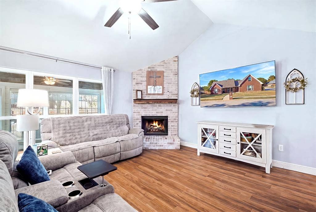 506 Amy Jo Circle, Aubrey, TX 76227 Vaulted ceiling with a ceiling fan, brick-clad fireplace with a wood mantle, wood-finish flooring, and large windows
