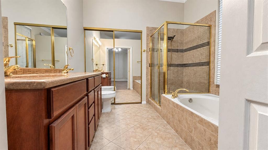 Dual wood-finish vanity with countertop, tiled flooring, built-in soaking tub, and enclosed shower with tile surround