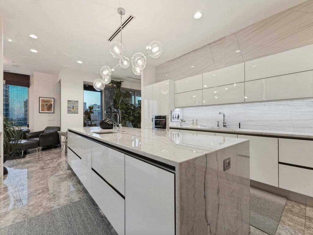 2300 Wolf Street, #14A, Dallas, TX 75201 Gourmet kitchen with a waterfall island, sleek white cabinetry, integrated sink, recessed lighting, and a contemporary chandelier