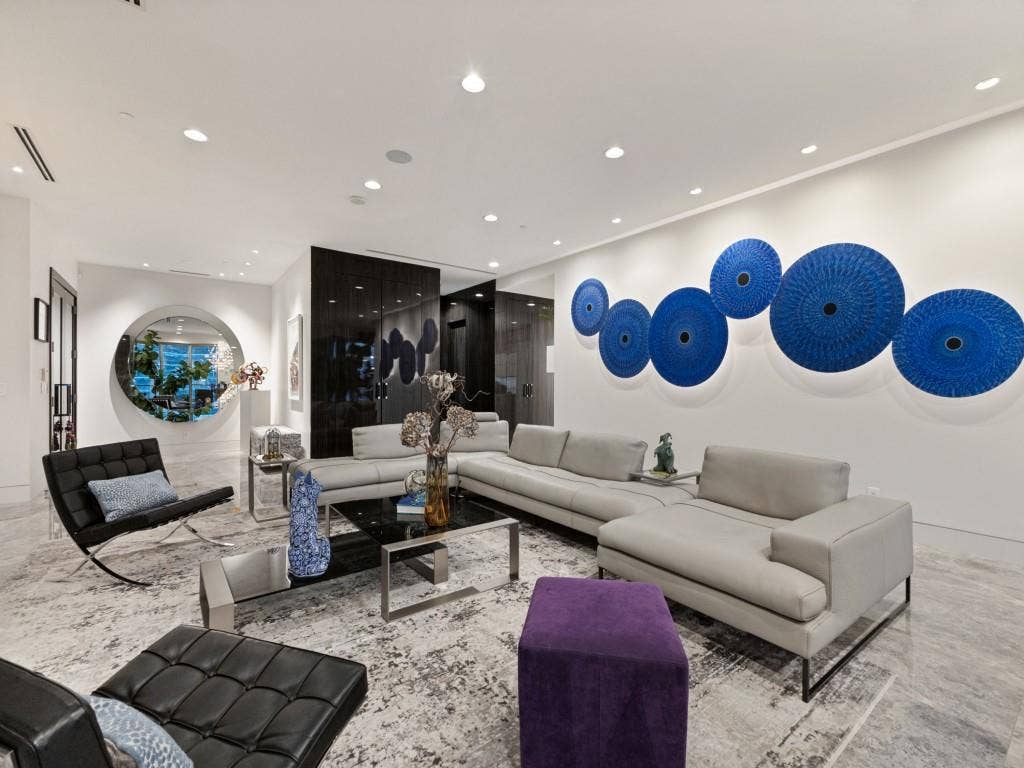 2300 Wolf Street, #14A, Dallas, TX 75201 Recessed lighting illuminates the expansive living area with high ceilings, featuring a large circular wall mirror and dark wood-finish paneling