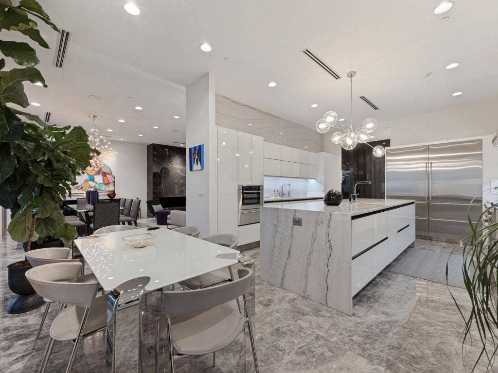 2300 Wolf Street, #14A, Dallas, TX 75201 Modern kitchen featuring high-gloss cabinetry, a central waterfall-edge island, stone-surfaced countertops, integrated stainless steel appliances, and recessed lighting