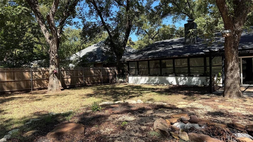 8513 Ravenswood Road, Granbury, TX 76049 Expansive backyard featuring a wood privacy fence, mature trees, and a stone-edged fire pit area
