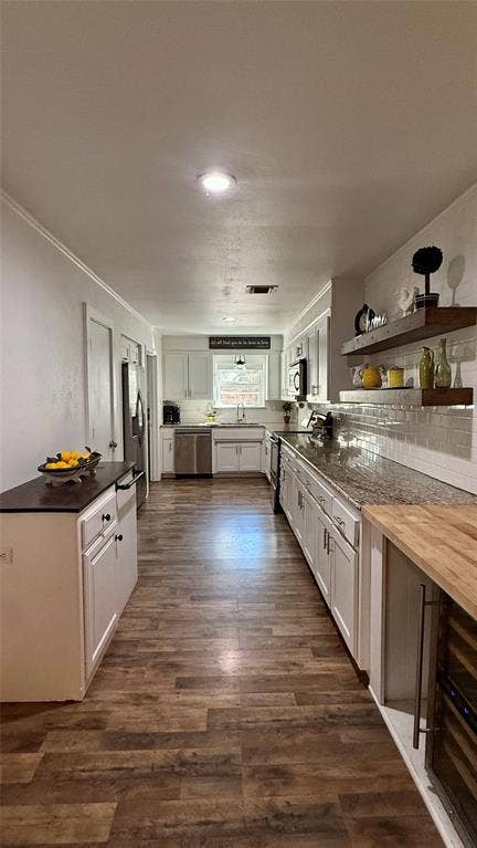 8513 Ravenswood Road, Granbury, TX 76049 Galley kitchen featuring wood-finish flooring, white cabinetry, granite-style countertops, stainless steel appliances, and a tile backsplash