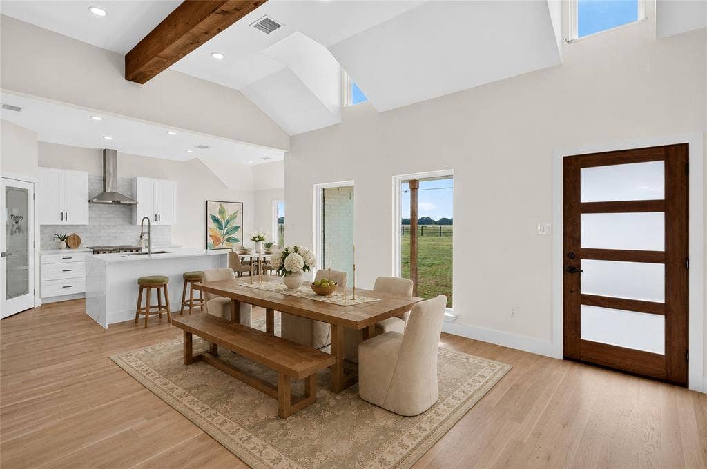 15166 FM 3133, Anna, TX 75409 Open-concept living space featuring vaulted ceilings with exposed wood beams, light wood-finish flooring, and white walls - Virtually Staged