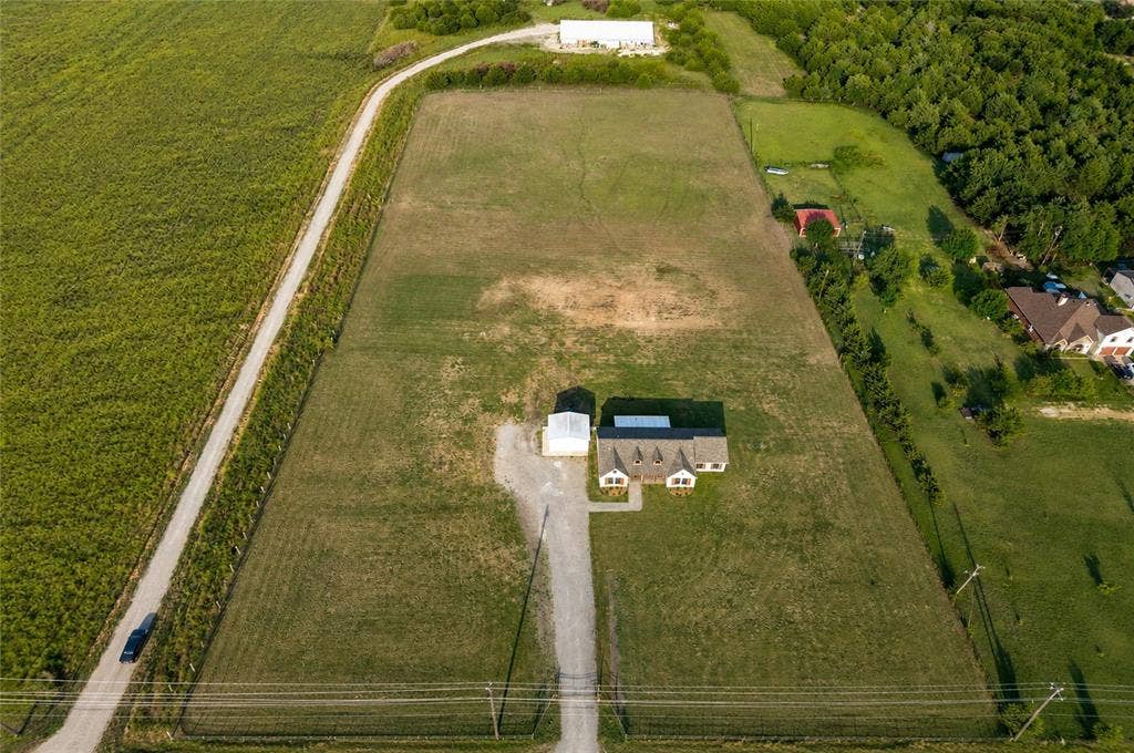 15166 FM 3133, Anna, TX 75409 Expansive land parcel featuring a residential structure, detached outbuilding, gravel driveway, and surrounding green fields