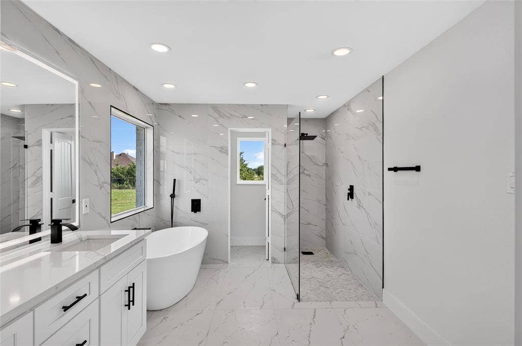15166 FM 3133, Anna, TX 75409 Modern bathroom featuring a freestanding soaking tub with a floor-mounted faucet, a spacious walk-in shower with glass partitions, a dual vanity with a white countertop and undermount sinks, and large-format tile flooring and wall accents