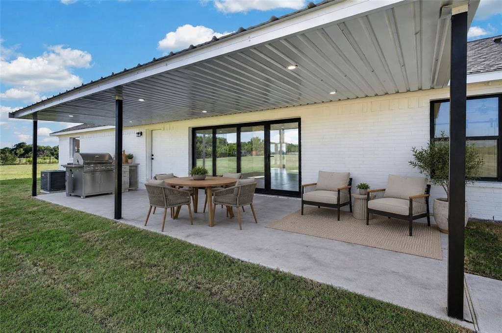 15166 FM 3133, Anna, TX 75409 Covered patio featuring a corrugated metal roof with recessed lighting, a white brick exterior, black-framed windows, and expansive sliding glass doors - Virtually Staged