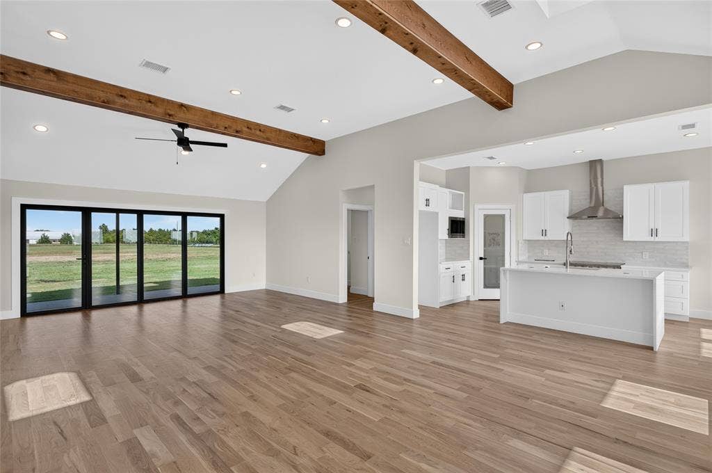 15166 FM 3133, Anna, TX 75409 Spacious living area featuring high vaulted ceilings with exposed wood beams, wood-finish flooring, and a contemporary ceiling fan