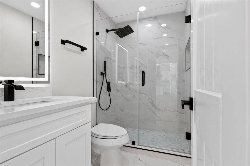15166 FM 3133, Anna, TX 75409 Bathroom featuring a walk-in shower with clear glass enclosure and black hardware, white vanity with quartz countertop, illuminated mirror, and black faucet