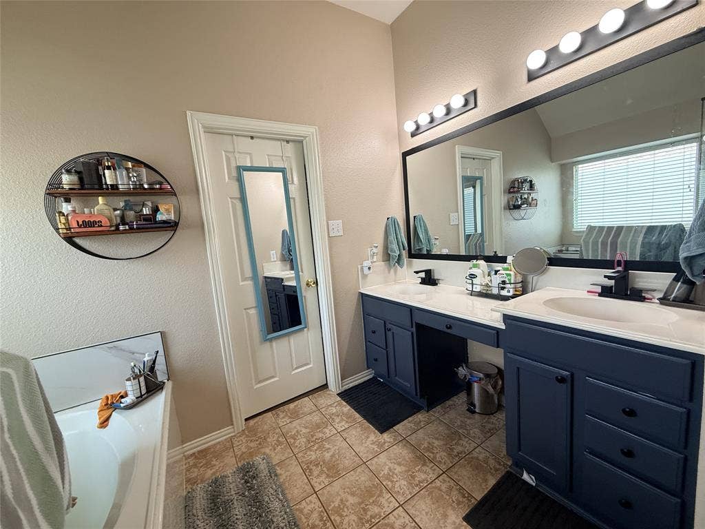 7004 Canyonbrook Drive, Plano, TX 75074 Dual vanity with integrated sinks and dark cabinetry, large wall-mounted mirror, overhead vanity lighting, and ceramic tile flooring