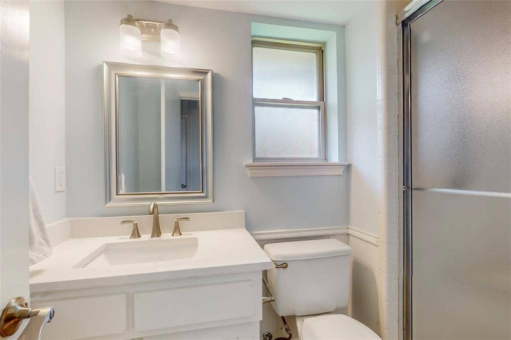 White vanity with integrated sink, brushed nickel faucet, framed mirror, and frosted glass shower enclosure