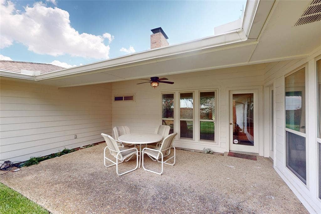 Covered patio with an exposed aggregate concrete surface, featuring a ceiling fan and a full-light glass door