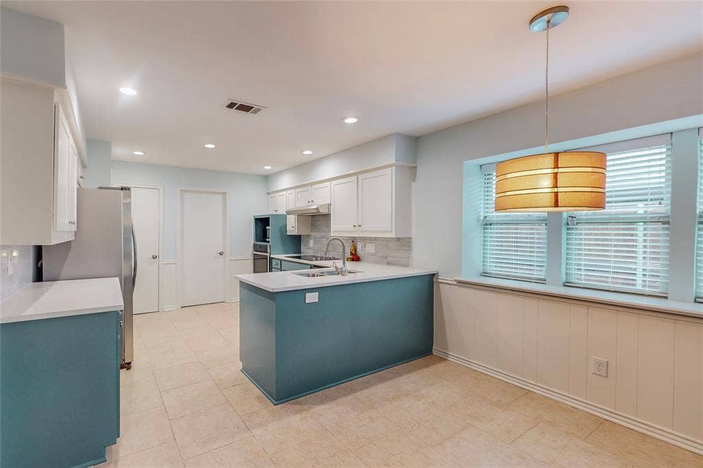 Kitchen featuring recessed lighting, an island with countertop, white upper cabinetry, a tile backsplash, and a pendant light fixture