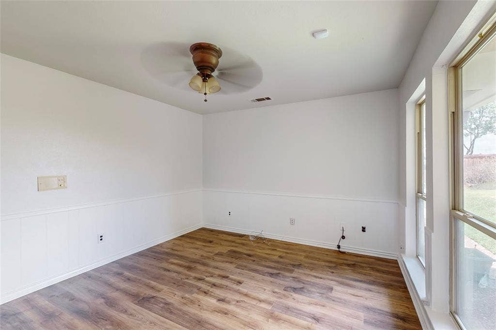 Wood-finish flooring, ceiling fan with light fixture, chair rail molding, and large windows