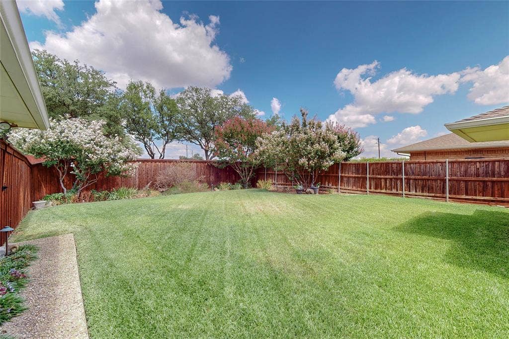 Expansive lawn area with a perimeter wood privacy fence, mature trees, and flowering shrubs