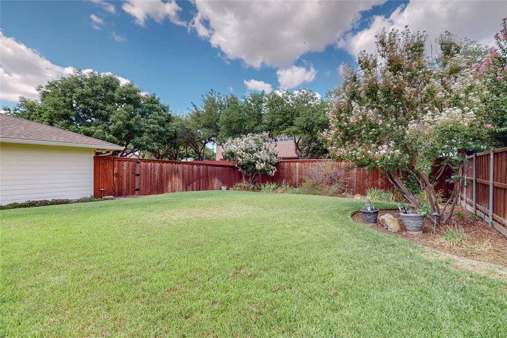 Manicured lawn with a privacy fence, mature trees, flowering shrubs, and planted beds