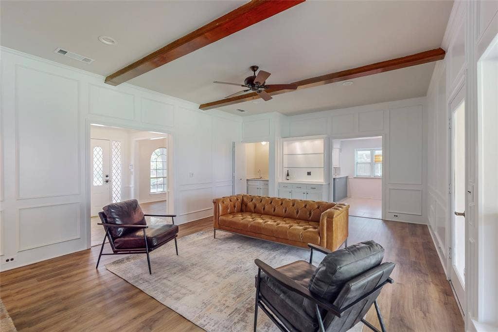 Wood-finish flooring, white paneled walls, exposed ceiling beams, recessed lighting, and a ceiling fan