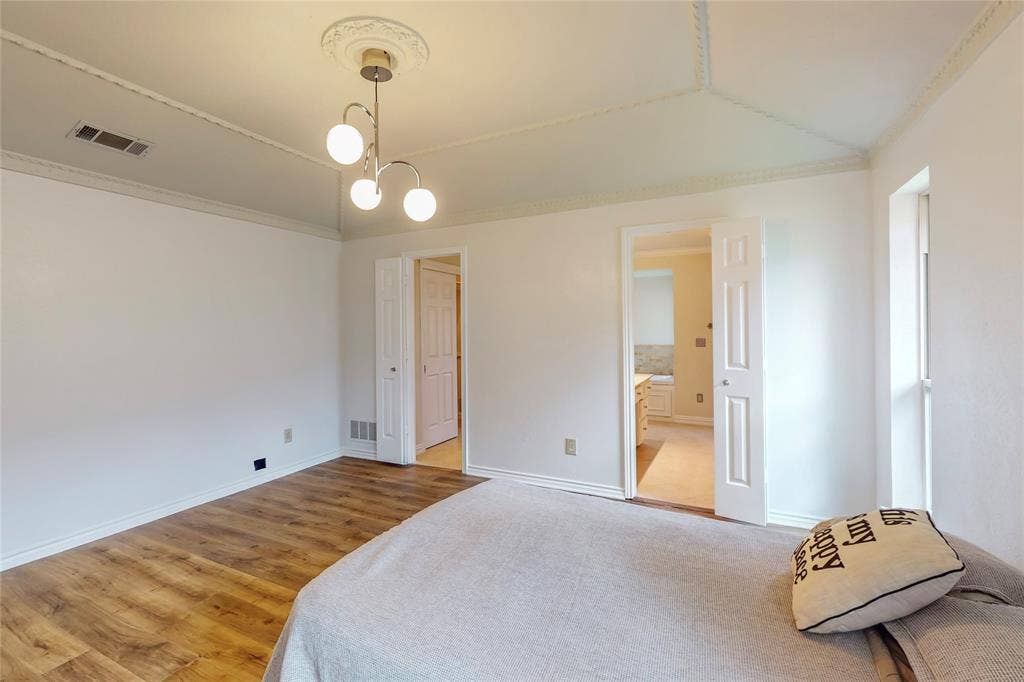 Wood-finish flooring with white baseboards, a vaulted ceiling with crown molding, and a decorative ceiling medallion with a contemporary light fixture