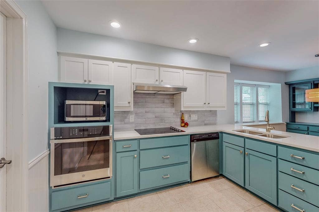 Kitchen featuring blue and white cabinetry, recessed lighting, stainless steel appliances, and a tiled backsplash
