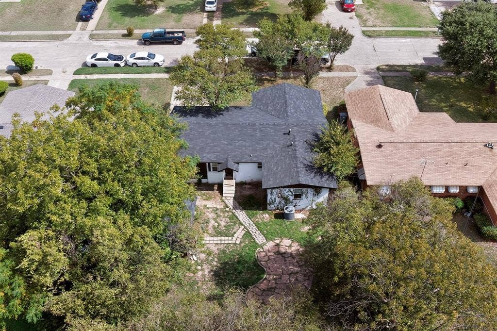 Aerial perspective of residential property featuring a pitched shingle roof, stone-paved walkway, and patterned stone patio, surrounded by mature trees