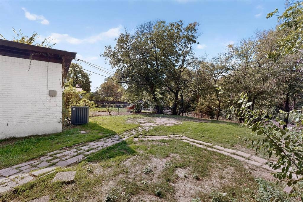 Backyard space featuring a white-painted brick exterior, natural grass lawn, mature trees, and stone-paver walkways