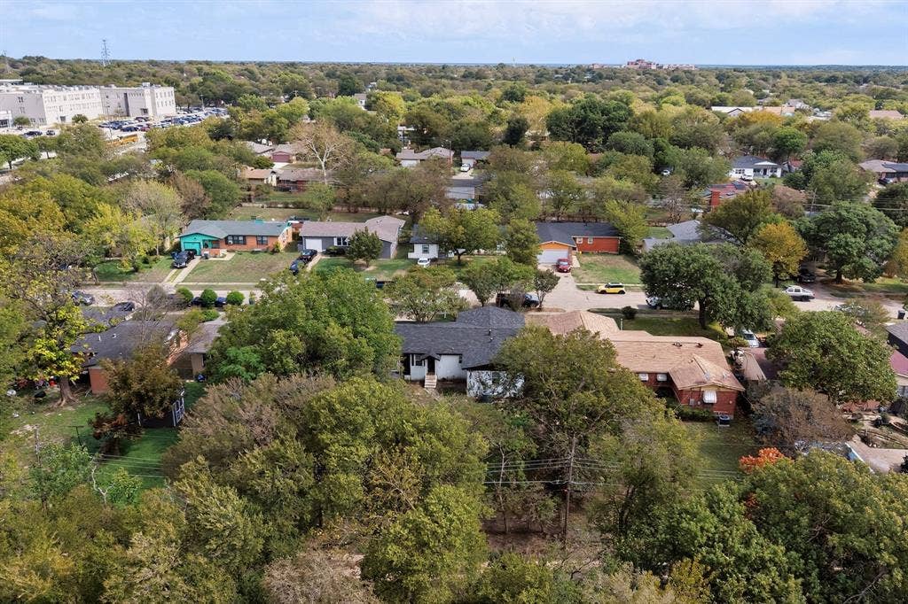 Aerial perspective of a residential lot featuring mature trees, expansive green space, and a multi-section roofline