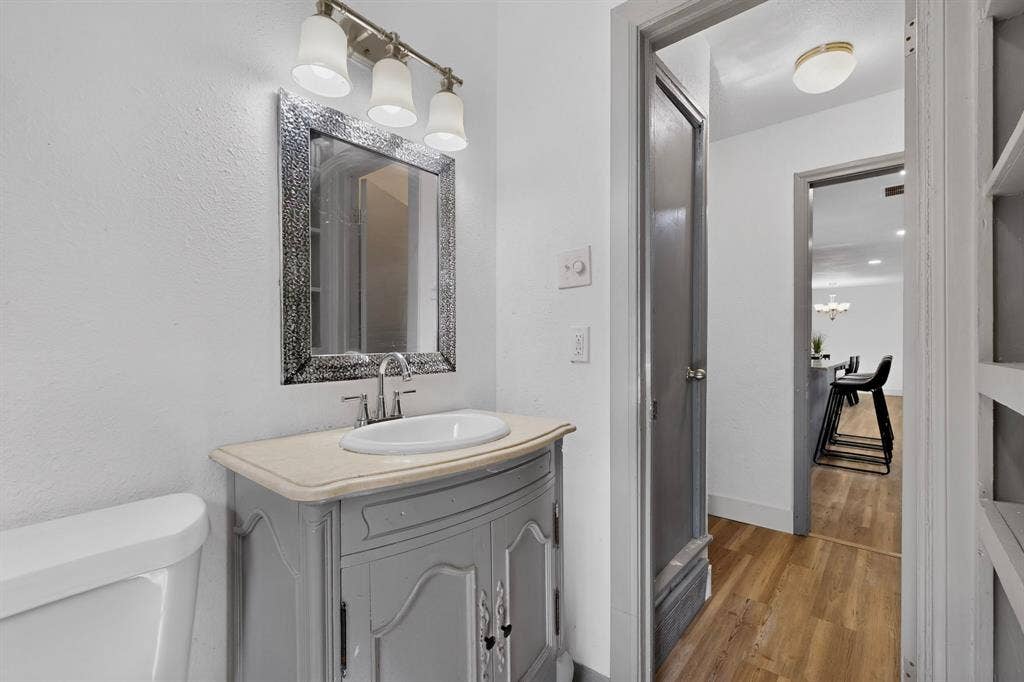 Vanity with a neutral-toned countertop and an integrated oval basin, complemented by a three-light vanity fixture and a decorative framed mirror