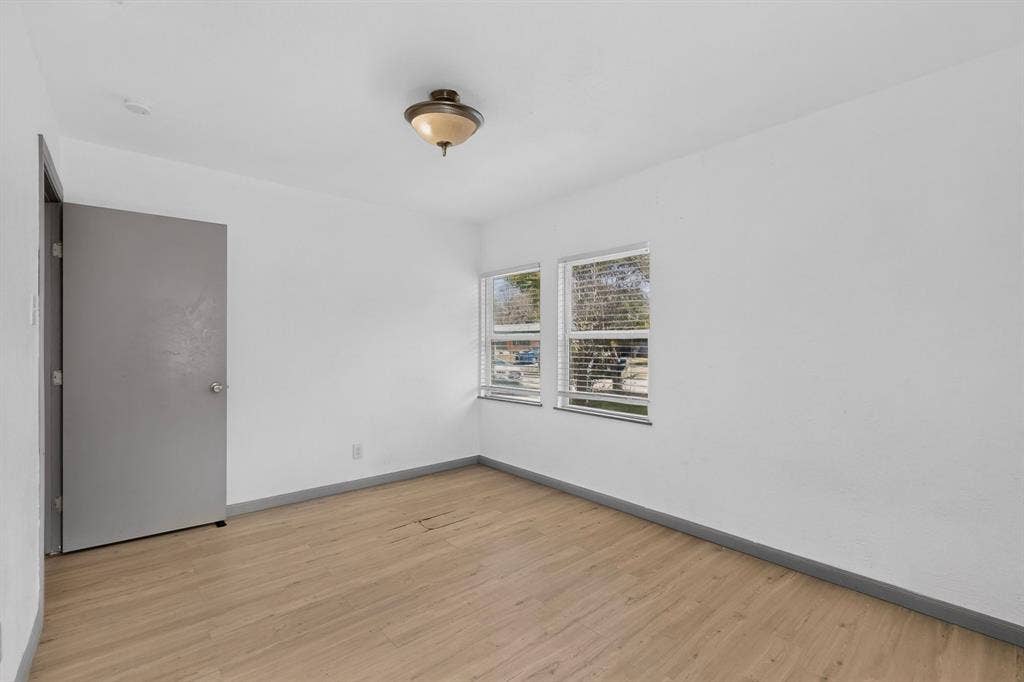 Interior space featuring wood-finish flooring, two dual-pane windows with horizontal blinds, and a neutral-toned interior door