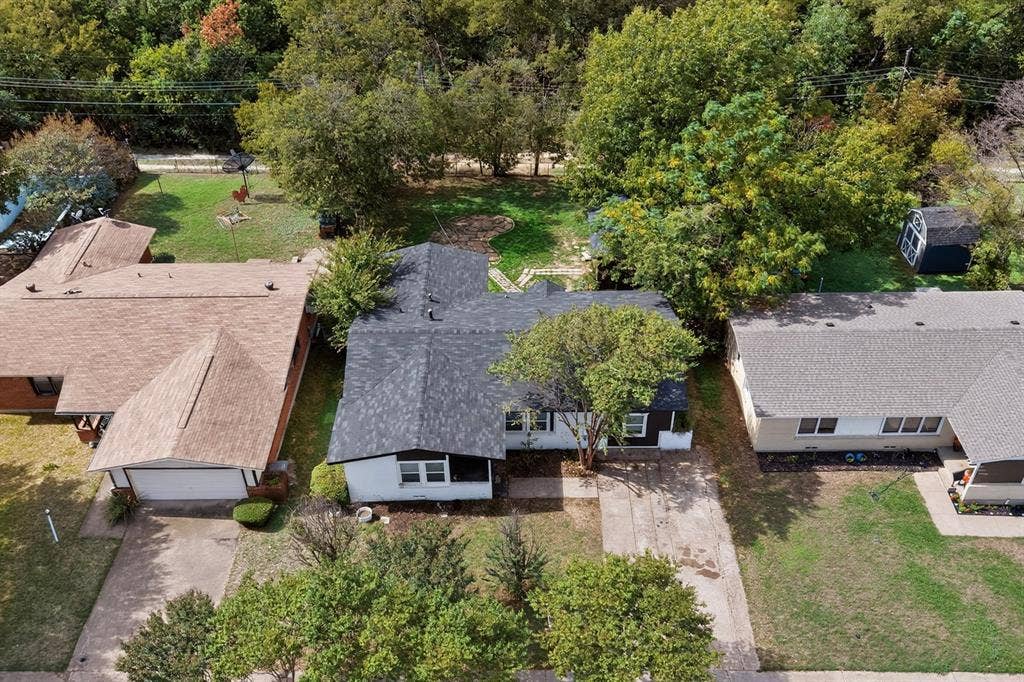 Aerial perspective of property featuring an expansive backyard, mature tree canopy, concrete driveway, and detached storage structure