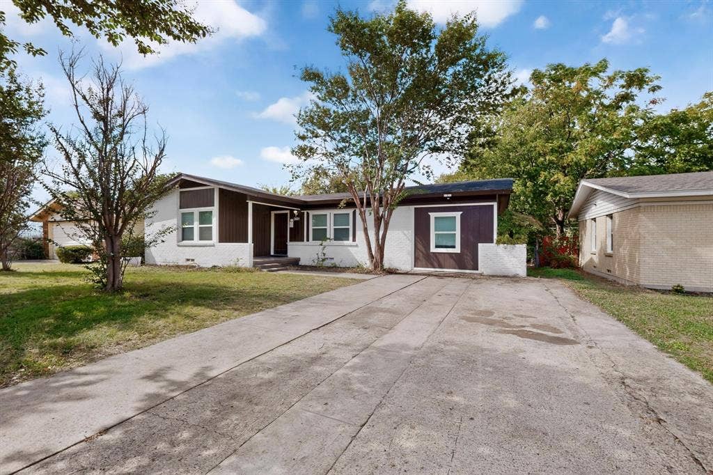 Single-story exterior featuring painted masonry and wood-panel siding, recessed entryway, multi-pane windows, and a concrete driveway