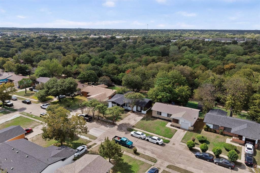 Aerial perspective featuring residential lots, paved streets, and a dense treeline backdrop