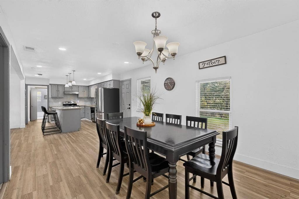 Open-concept interior featuring wood-finish flooring, recessed lighting, a multi-arm chandelier, and a kitchen island with stone-finish countertops