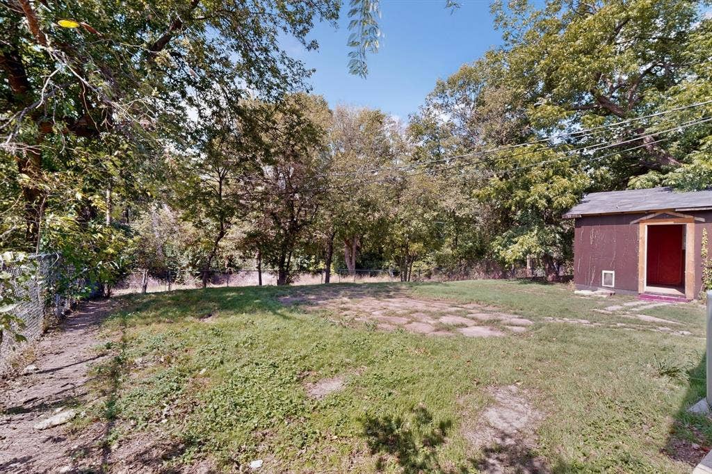 Backyard featuring a grass lawn, stone paver path, mature trees, chain-link fencing, and a detached outbuilding