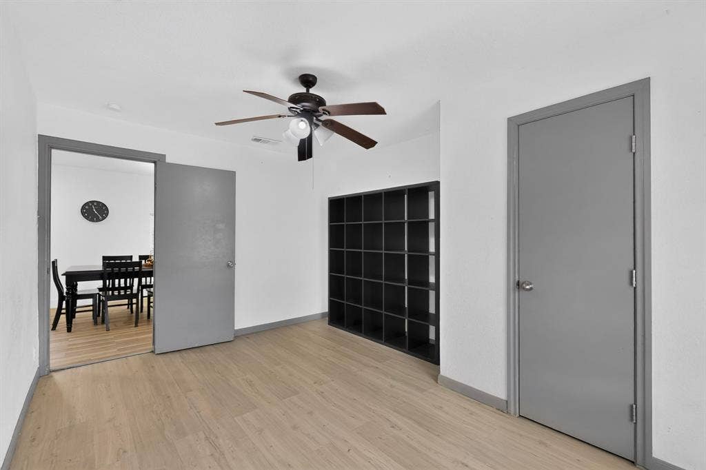 Interior space featuring wood-finish flooring, a built-in dark shelving unit, and a ceiling-mounted light fixture with a fan