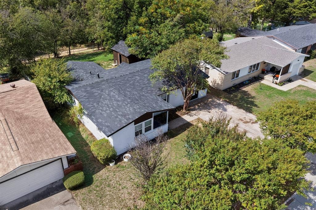 Aerial perspective featuring single-story structures with dark shingle roofing, exterior light-toned siding, attached garages, and mature tree-lined grounds