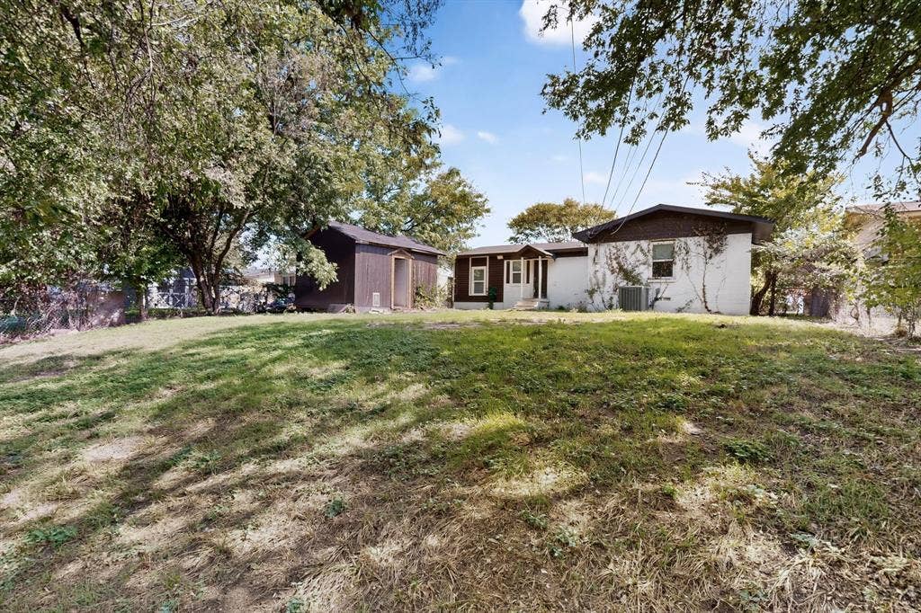 Exterior featuring a white painted brick finish, an attached storage shed, and a sloped lot with mature trees