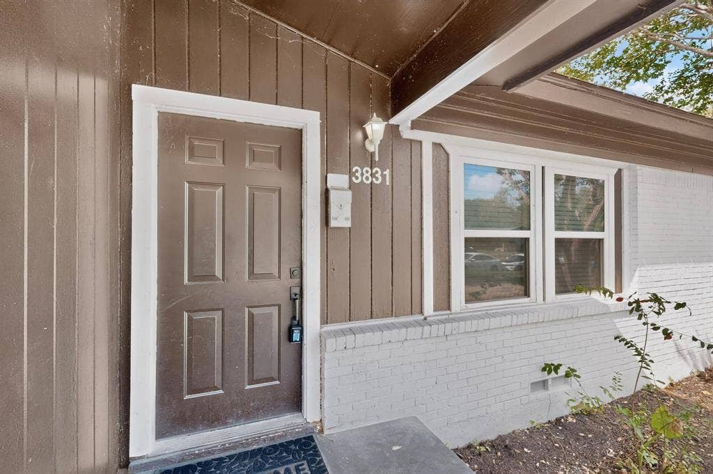 Entryway featuring vertical wood-finish siding, a painted brick facade, six-panel door, double-hung windows, and exterior sconce lighting