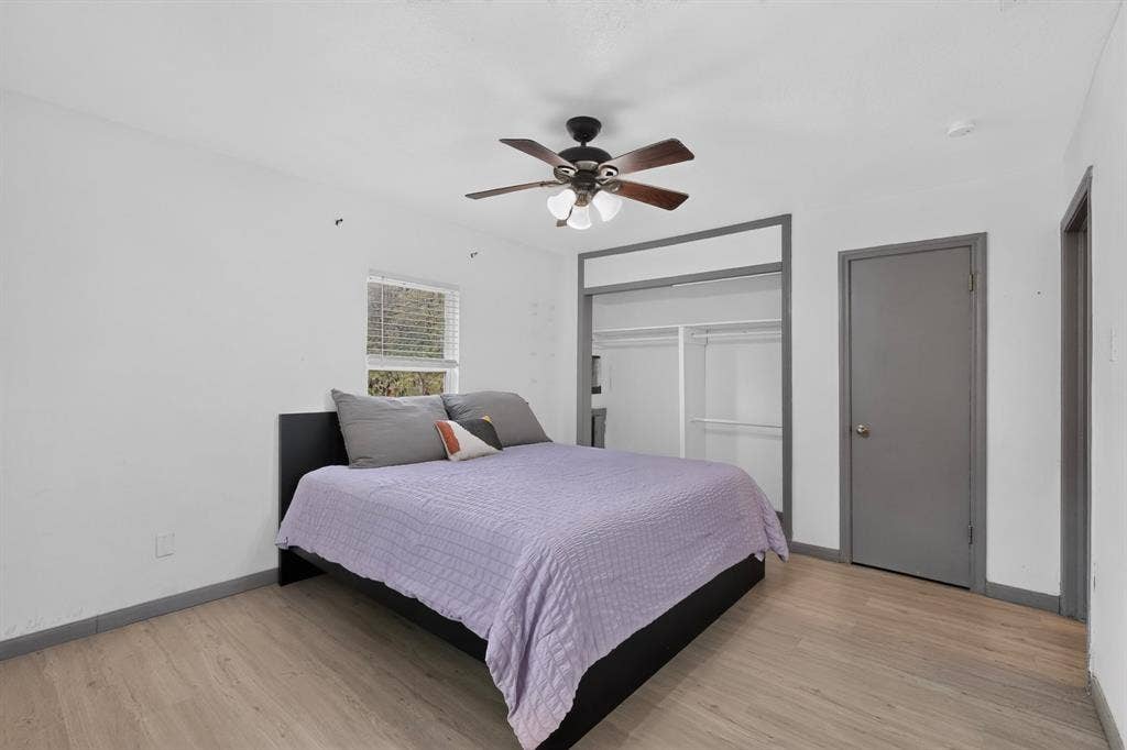 Room featuring wood-finish flooring, a ceiling fan with integrated lighting, a sliding door closet with framing, and a window with blinds