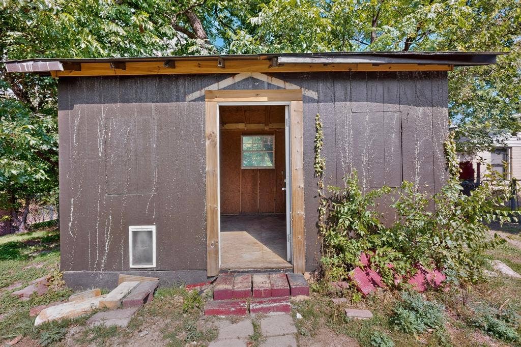 Detached shed featuring wood-panel siding, a single-entry doorway, a multi-pane window, and an integrated pet door