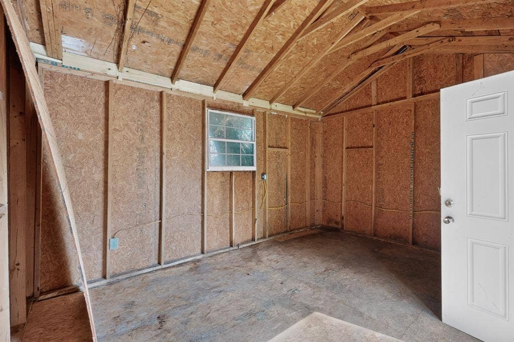 Outbuilding interior featuring exposed wood-stud framing, vaulted roof rafters, a single-hung window, and an exterior-grade door