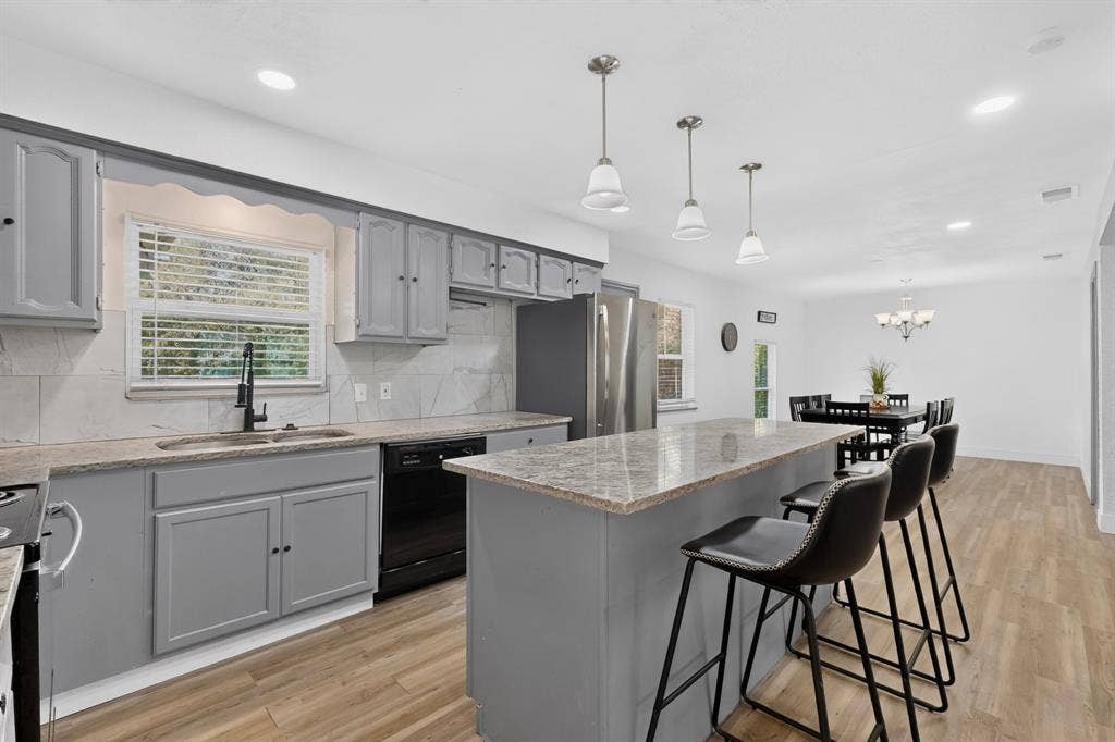Kitchen featuring grey cabinetry, stone-finish countertops, an island with bar seating, wood-finish flooring, and recessed lighting