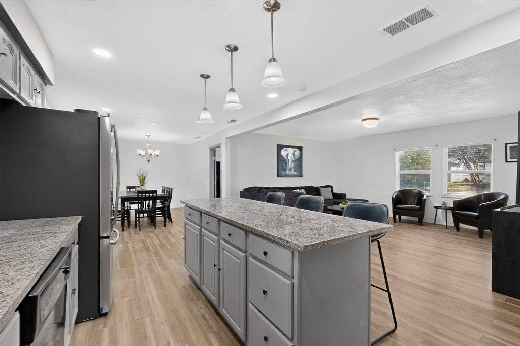 Kitchen featuring a central island with stone-finish countertops, grey cabinetry, stainless steel appliances, and pendant lighting over wood-finish flooring