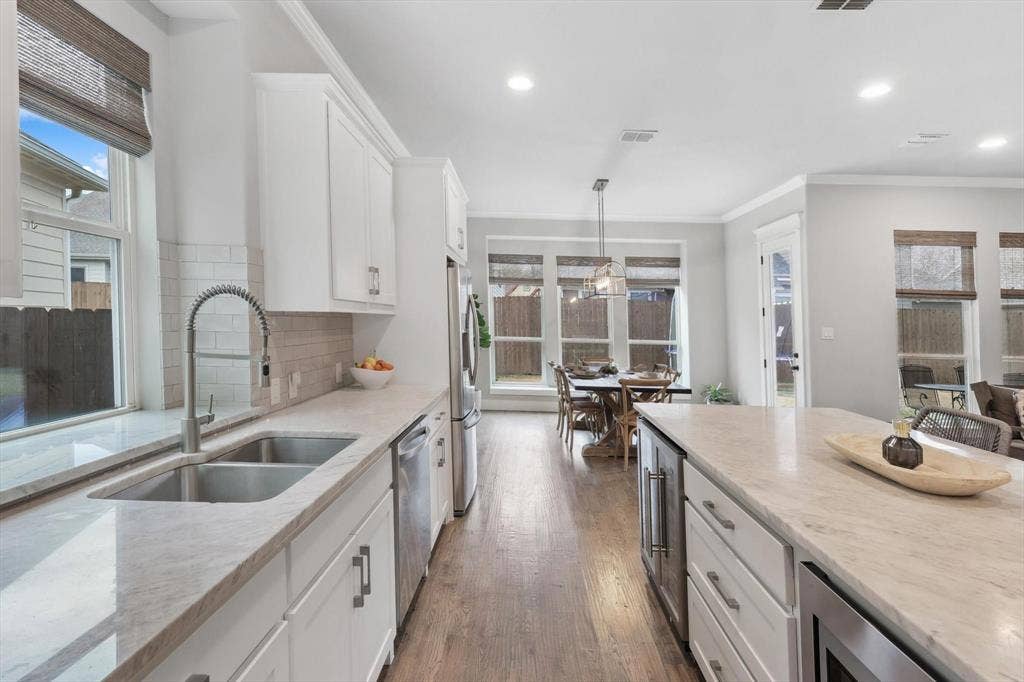 Kitchen featuring a double basin stainless steel sink with a gooseneck faucet, light-toned countertops, and wood-finish flooring