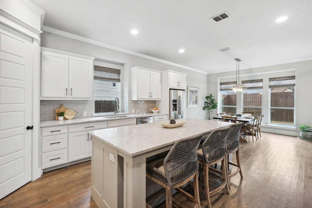 Kitchen featuring white cabinetry, light-colored countertops, stainless steel appliances, a center island with seating, and wood-finish flooring