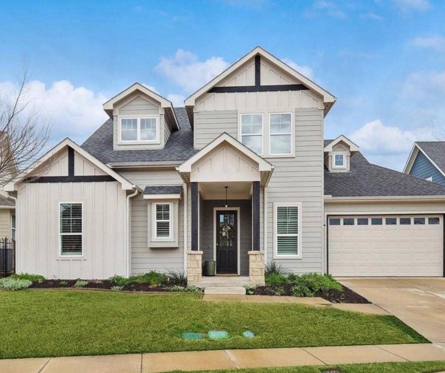 Gabled roofline with dormer windows, stone column accents, covered entry, attached garage, and manicured front landscaping