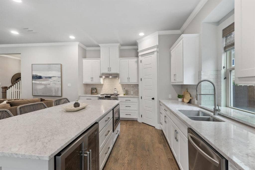Kitchen featuring a large island with integrated beverage cooler, stainless steel appliances, white cabinetry, and wood-finish flooring